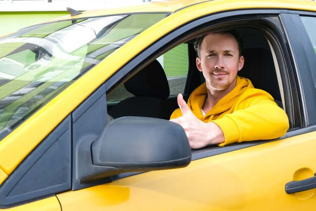 taxi driver in a yellow hoodie giving a thumbs-up inside a taxi.