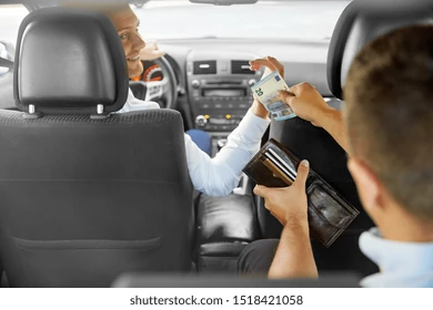 Passenger handing cash to taxi driver with wallet in hand.