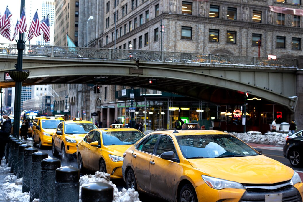 four New York city cabs below the bridge on the city street during daytime