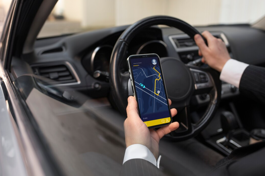 A driver's hand holding a smartphone displaying a GPS navigation route inside a car.